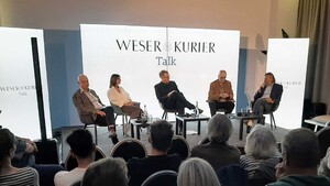 Fünf Personen bei einer Podiumsdiskussion vor dem Logo des Weser-Kurier. Publikum im Vordergrund